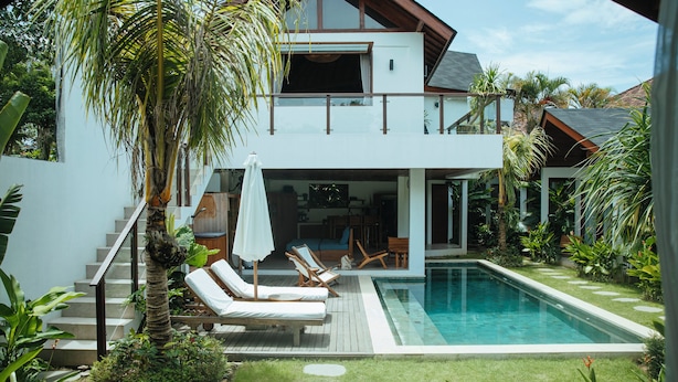 Une maison moderne à deux étages dotée d’une piscine, d’un espace extérieur aménagé et d’une végétation luxuriante.