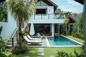 Et moderne hus med to etager, en swimmingpool, udendørs siddepladser og frodig beplantning.