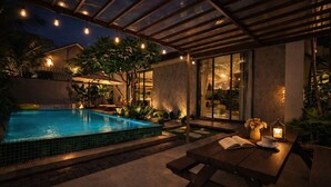 Ein Schwimmbad mit Glasdach, umgeben von Pflanzen und einer Terrasse mit Tisch und Stühlen.