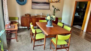 Een eethoek met een houten tafel en groene stoelen, een vaas met bloemen en een blauw bord aan de muur.