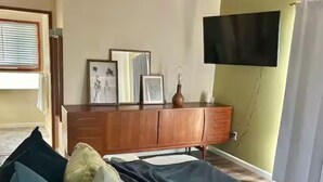 Een slaapkamer met een bed, een houten dressoir, een flatscreen-tv aan de wand en een raam met zonwering.
