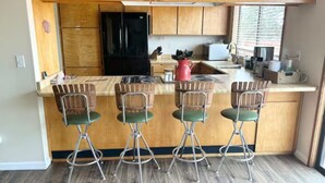 Een keuken met houten kasten, een zwarte koelkast, een fornuis en vier barstoelen.