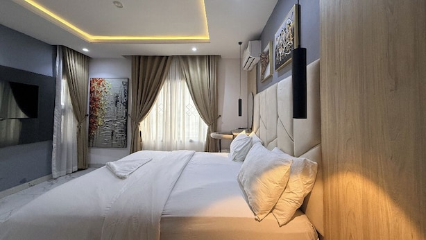 A modern hotel room with a large bed, a flat-screen TV, and a painting on the wall. - Spacious 3-bedroom apartment in Victoria Island - VI, Lagos (Lagos)