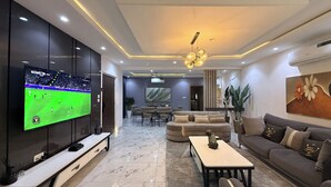 A modern living room with a flat-screen TV, a sofa, a coffee table, and a dining area with chairs. - Spacious 3-bedroom apartment in Victoria Island - VI, Lagos (Lagos)
