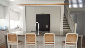 Une cuisine moderne dotée d’un îlot central, de tabourets de bar blancs et d’un escalier menant à un niveau supérieur.