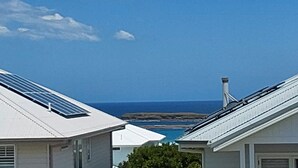 Un quartier résidentiel situé sur la côte, où les maisons sont dotées de panneaux solaires sur les toits, le ciel est d’un bleu éclatant et on peut admirer l’océan.