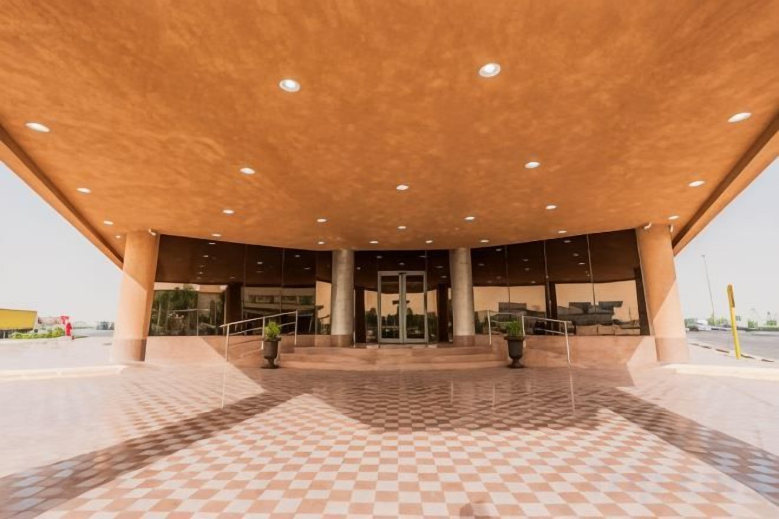 Entrada de un edificio con piso de patrón de cuadros, una zona techada con techo de madera y una puerta central.