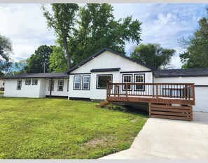 A single-story house with a front deck, a garage, and a well-maintained lawn.