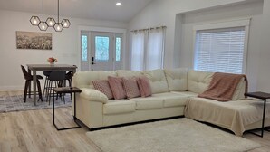 A modern living room with a sectional sofa, a dining table, and a ceiling fan. - Modern & open 3-bedroom house with 3 stall garage in a perfect location.. (Ventura)