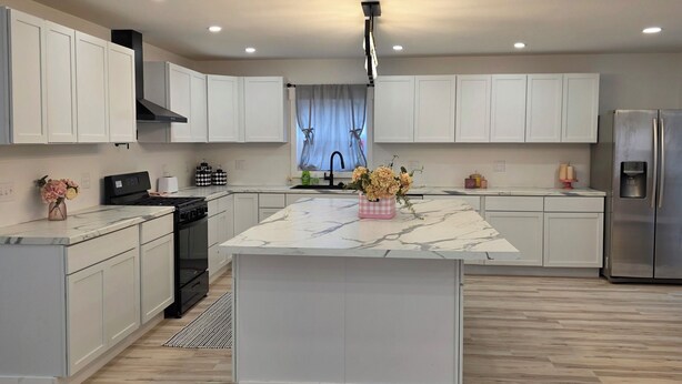 A modern kitchen with white cabinets, a central island, a stainless steel refrigerator, and a black stove. - Modern & open 3-bedroom house with 3 stall garage in a perfect location.. (Ventura)