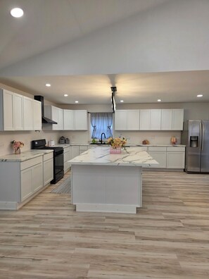 A modern kitchen with white cabinets, a central island, a stainless steel refrigerator, and a black stove.
