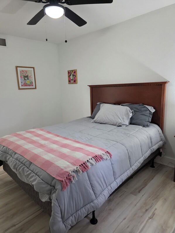 A bedroom with a bed, a ceiling fan, and two wall-mounted pictures.