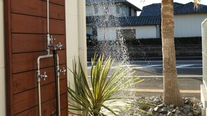A showerhead with water flowing, a wooden door, and a palm tree. - Villa with a Natural Spring Bath and Wood-Fired Sauna — Aoshima (宮崎市青島)
