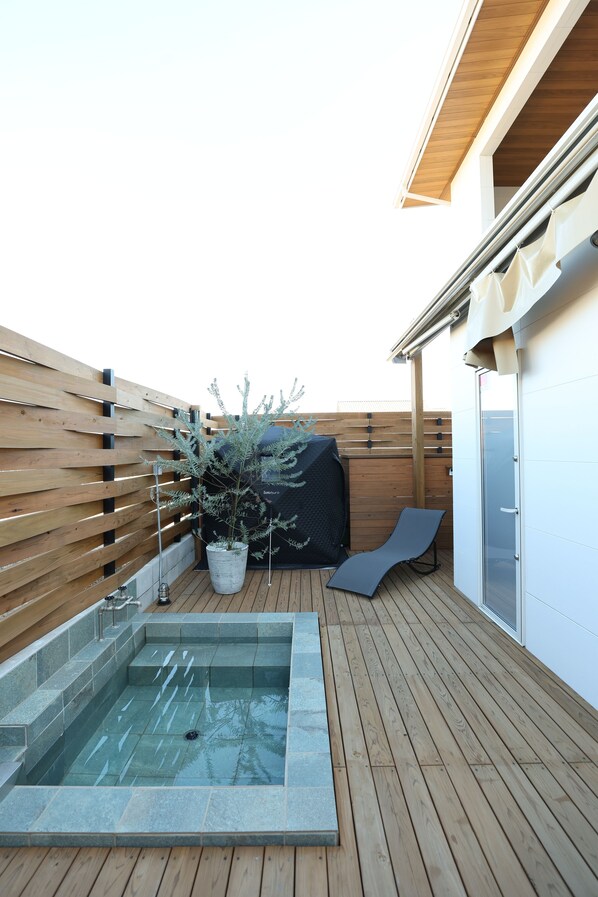 Una terraza en la azotea con jacuzzi, una planta en maceta y una tumbona.