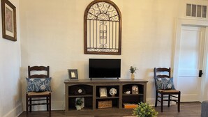 A living room with a wooden entertainment unit, two chairs, a television, and a decorative window.