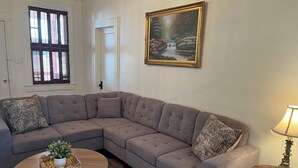 A living room with a sectional sofa, a small round table, a lamp, and a painting on the wall.