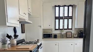 A kitchen with white cabinets, a microwave, a coffee maker, and a window with blinds.