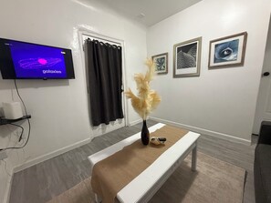 Una habitación con televisión mostrando una imagen de galaxia, un banco, un florero con plantas secas y cuadros en la pared.