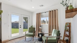 Ein Zimmer mit einer Schiebetür zum Garten, zwei grüne Sessel, ein kleiner runder Tisch, eine Lampe, ein Holzregal mit Pflanzen und ein Globus.