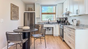 Een moderne keuken met witte kasten, roestvrijstalen apparatuur en een eethoek met een ronde tafel en stoelen.