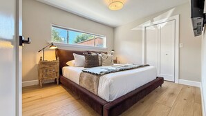 Een slaapkamer met een groot bed, een nachtkastje, een raam en een deur.