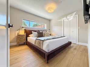 Un dormitorio con una cama grande, una mesita de noche, una ventana y una puerta.