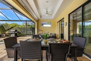Un patio al aire libre con mobiliario de mimbre, una mesa de comedor con platos y un ventilador de techo.