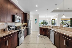 A modern kitchen with dark wood cabinets, stainless steel appliances, and a marble countertop. - NEW LISTING: Relaxing Escape! Waterfront Heated Pool Oasis (Cape Coral)