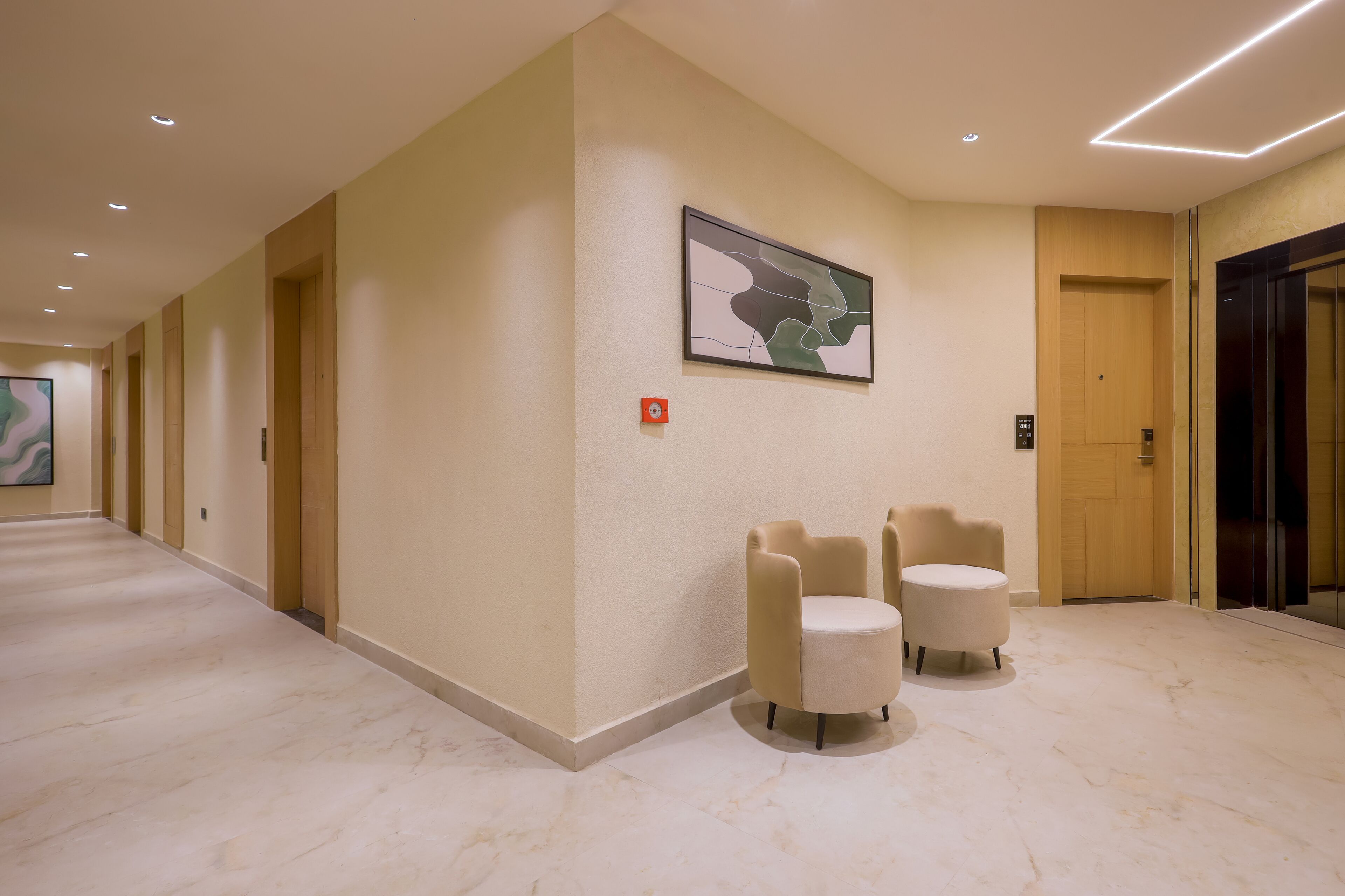 A hotel lobby with a marble floor, a reception desk, a wall-mounted abstract painting, and a glass elevator.