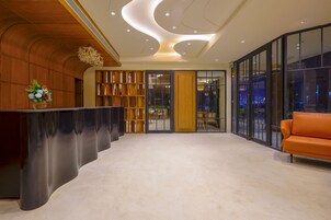 Un área de recepción moderna con un mostrador curvo, una estantería de madera y un separador de vidrio.