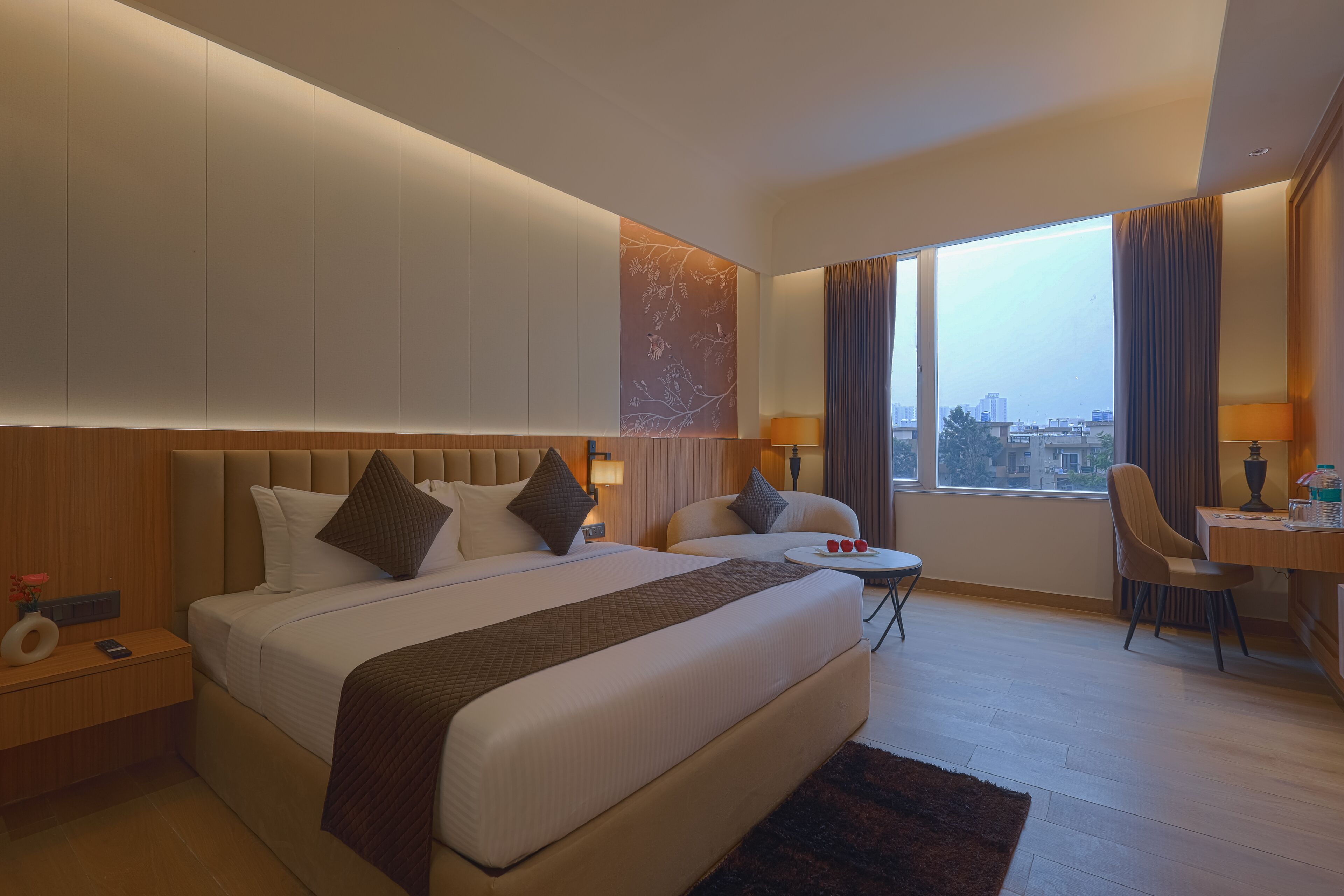 A modern hotel room with a large bed, a desk, a chair, and a view of the city.