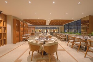Un restaurante espacioso con varias mesas y sillas, estantes de madera y un diseño de techo moderno.