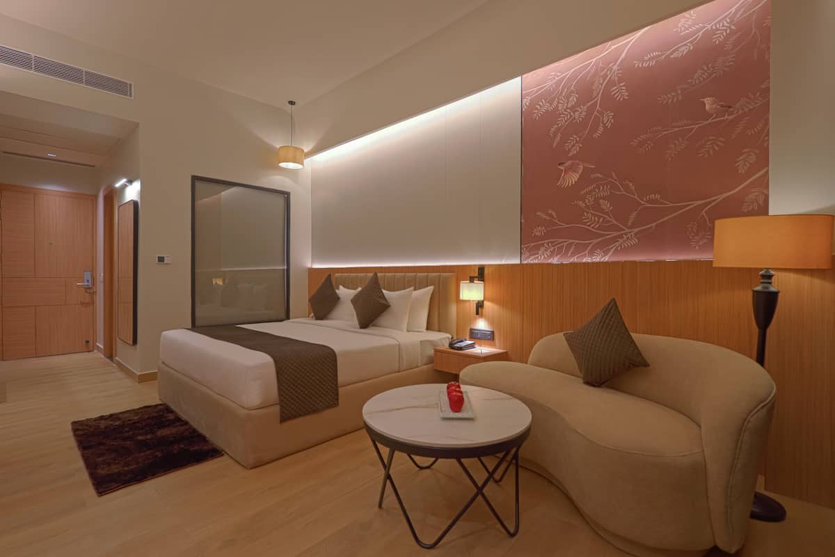 A hotel room with a bed, a sofa, a small table, and a nightstand with a lamp.