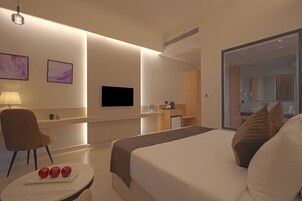 Una habitación de hotel moderna con cama, escritorio, silla, televisión y baño visible a través de una puerta de cristal.