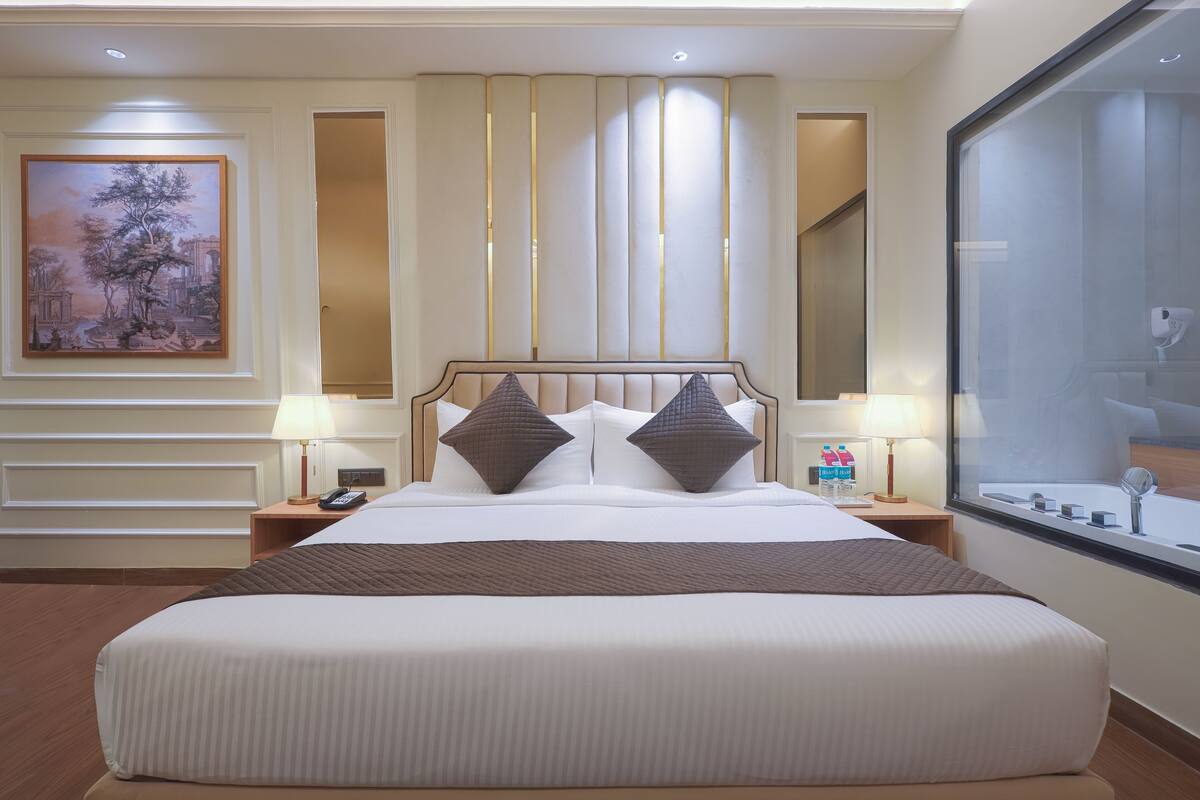 A large bed with a headboard, two bedside tables with lamps, a painting on the wall, and a large window.