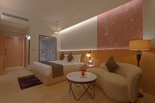 Una habitación de hotel moderna con una cama, un sofá, una mesita pequeña y una mesita de noche.