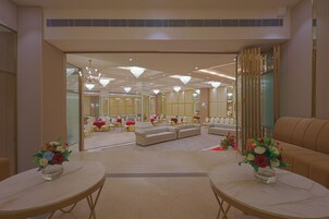 Un amplio vestíbulo de hotel con un área de estar central, varias mesas y un espejo grande que refleja la sala.
