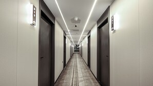 Ein langer, schmaler Hotelkorridor mit Türen an beiden Seiten, Deckenbeleuchtung und Teppichboden.