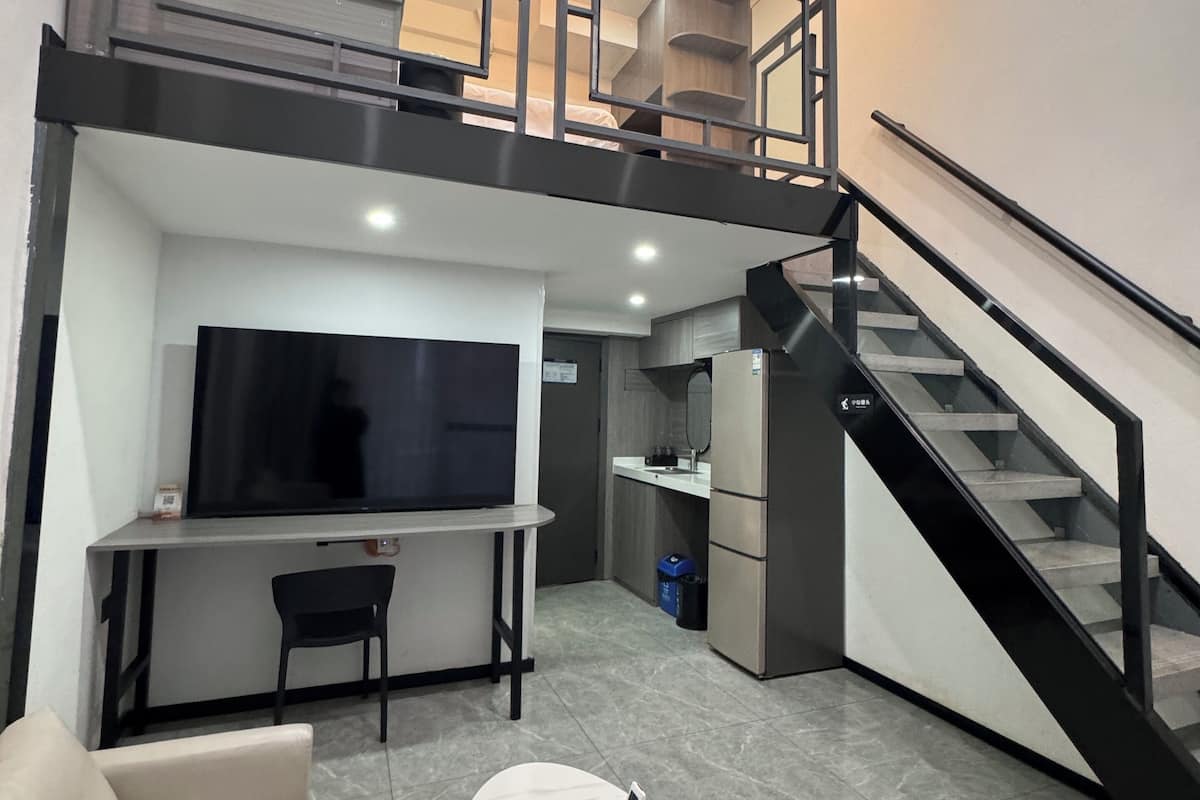 Un saló modern amb un sofà, una taula de centre, televisió, una escala i una zona de cuina.