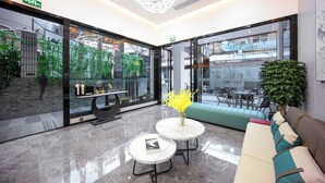 Eine moderne Lobby mit Glaswänden, einem Empfangsbereich, einer Sitzecke und einer großen Pflanze.