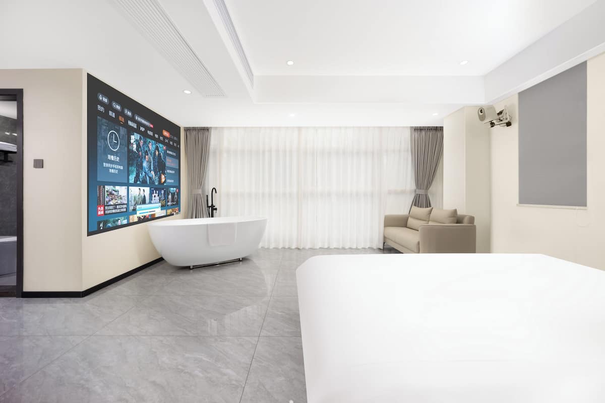 Habitació d'hotel moderna amb un llit gran, una banyera independent, un sofà i una televisió penjada a la paret que mostra diferents continguts.