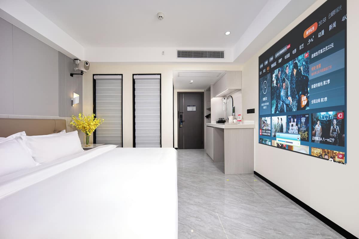 Habitació d'hotel amb un llit, escriptori i una gran pantalla digital que mostra diversos continguts.