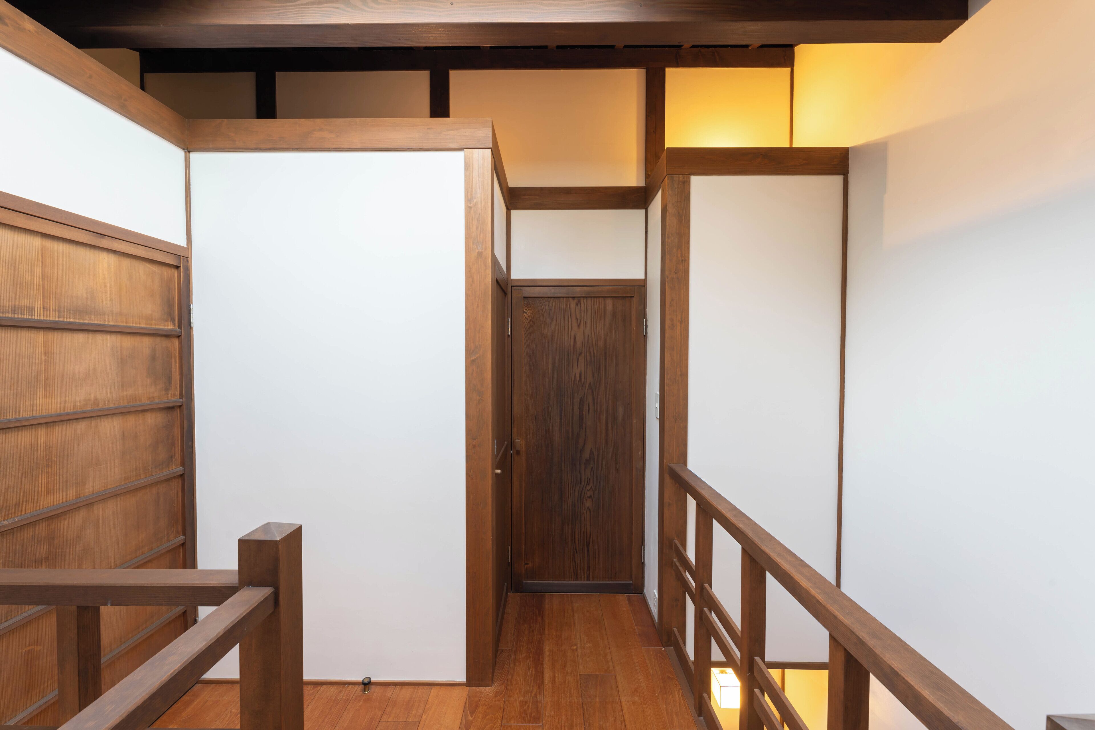 Una escalera de madera estrecha con barandilla de madera, que lleva a una puerta en la parte superior.