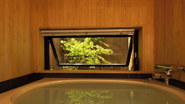 A wooden-paneled room with a large oval bathtub and a window overlooking a green tree. - Quiet Gion Machiya:Private Tea Room&Matcha Experience.Illuminated Courtyard Bath (京都市)