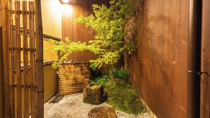 A traditional Japanese garden with a wooden fence, a bamboo gate, a moss-covered rock, and a small tree. - Quiet Gion Machiya:Private Tea Room&Matcha Experience.Illuminated Courtyard Bath (京都市)