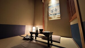 A traditional Japanese room with tatami flooring, a low table, a cushion, and a shoji screen with calligraphy. - Quiet Gion Machiya:Private Tea Room&Matcha Experience.Illuminated Courtyard Bath (京都市)