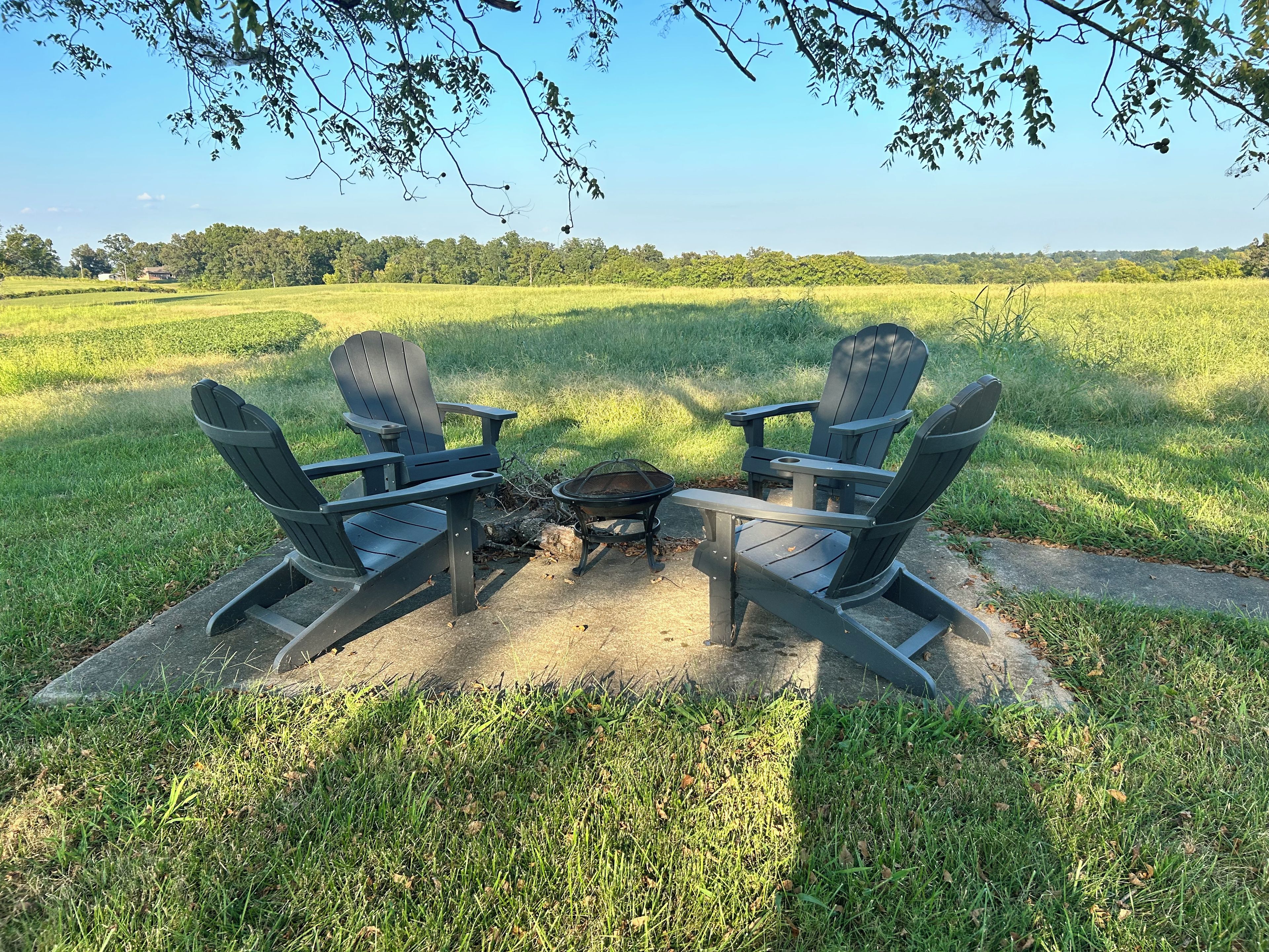 Two Adirondack chairs facing each other with a fire pit between them in a grassy field.