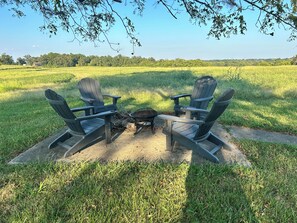 Two Adirondack chairs facing each other with a fire pit between them in a grassy field.