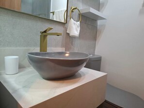 Een moderne badkamer met een grote wastafel, een gouden kraan, een witte handdoek en een witte beker op het aanrecht.