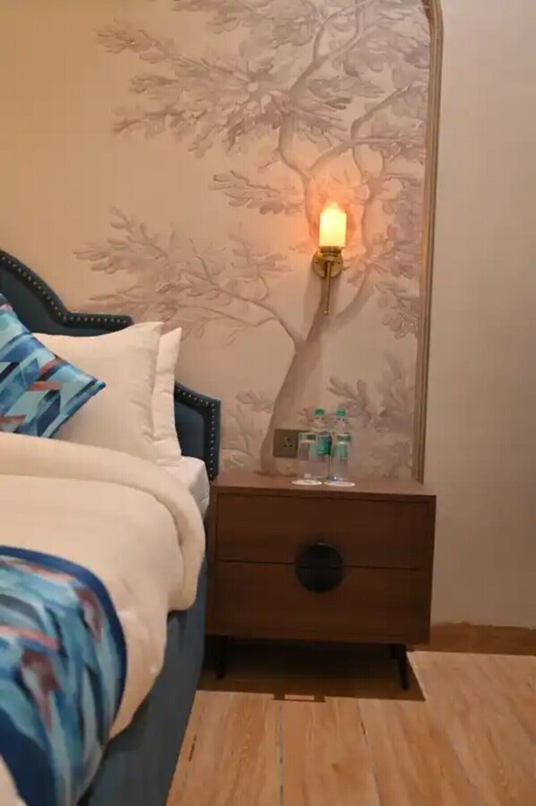A bedroom with a bed, a nightstand with a lamp, and a wall with a tree mural. - Hotel Phantom (Ganganagar)